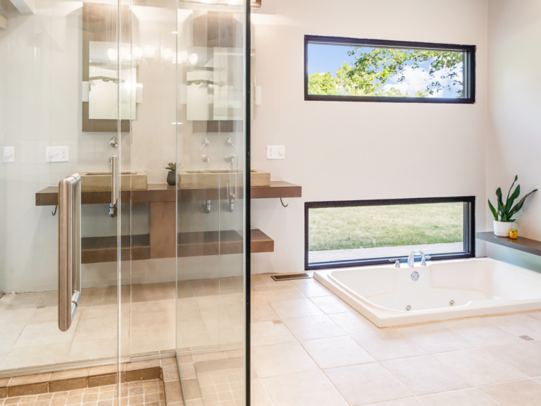 Glass shower, sunken soaking tub, and horizontal feature windows of primary bathroom in modern renovation home project by The RBT Group.