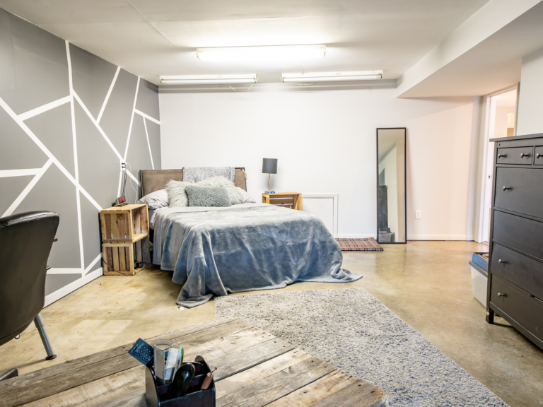 Large secondary bedroom in modern renovation home project by The RBT Group featuring painted feature wall and sealed concrete floors.